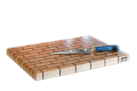 large maple brick pattern end grain cutting board on white background with chef knife resting on surface.